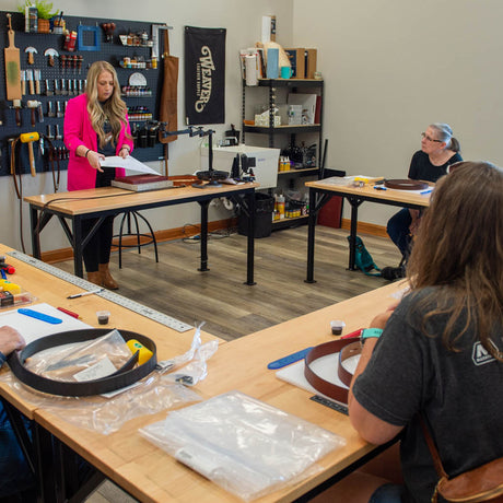Instructor leading a leathercraft class at Weaver Leather Supply with students seated at workbenches.