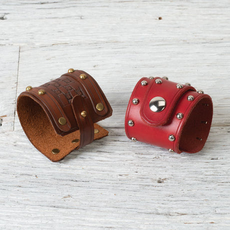Two stylish leather cuffs: one brown with gold studs and woven design, the other red with silver studs and a central snap.