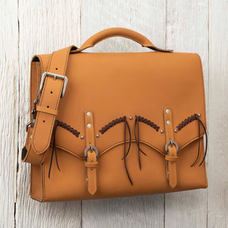 A stylish tan leather bag with braided detailing and metal accents, resting on a wooden surface.