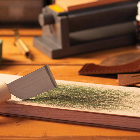 Leathercraft knife being sharpened on a strop coated with green compound.