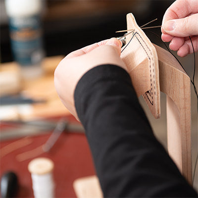 Person hand stitching leather using a stitching pony for support.