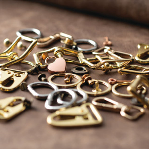 Assorted leathercraft hardware including buckles, rings, clasps, and a small heart charm on a leather surface.