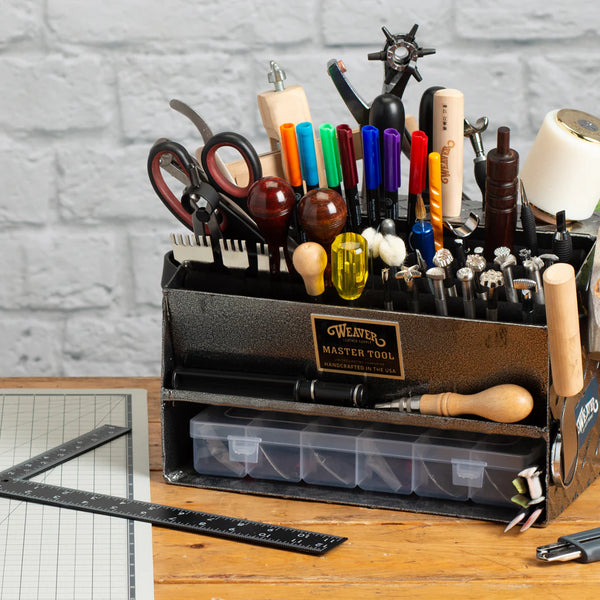 Weaver Master Tool organizer filled with leathercraft tools, stamps, scissors, awls, and markers on a workbench.
