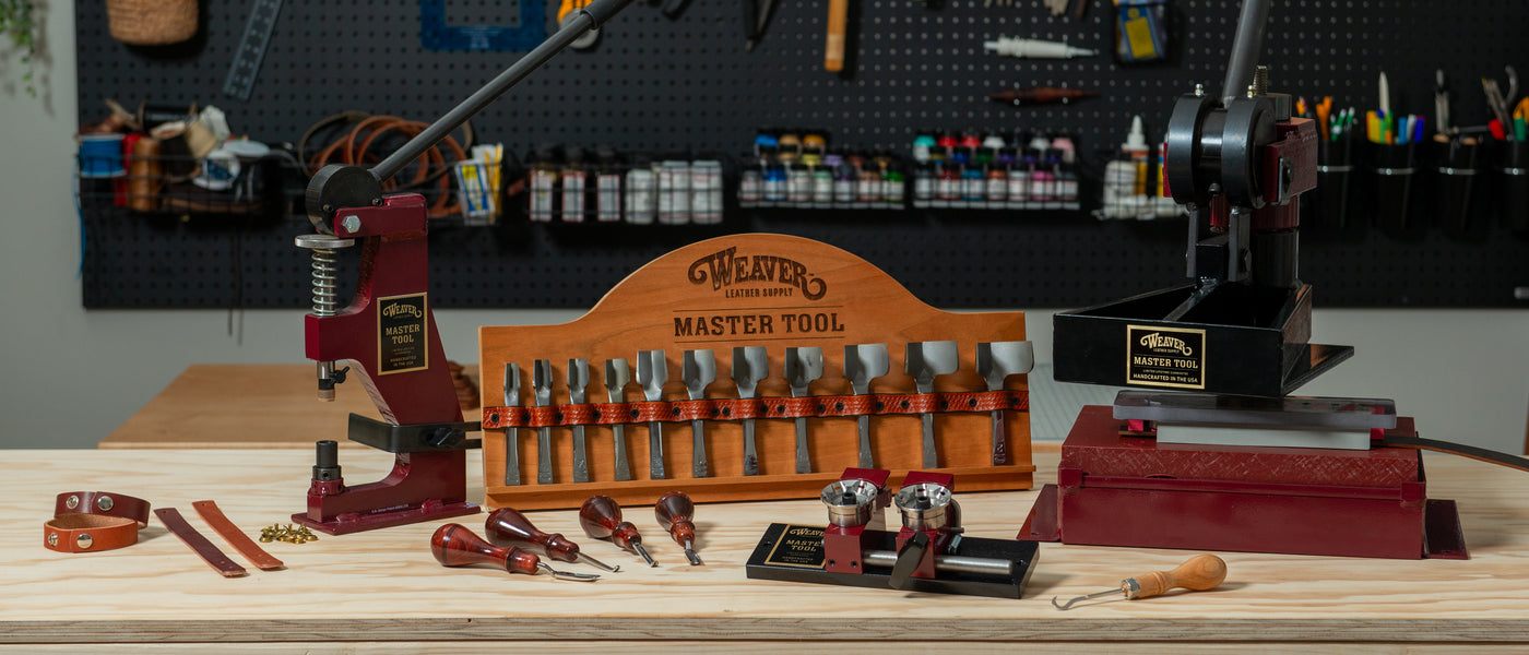 Leatherworking tools and machinery from Weaver Leather Supply displayed on a wooden workbench, including Master Tool presses, edgers, strap cutters, and punches arranged neatly with leather straps and hardware.
