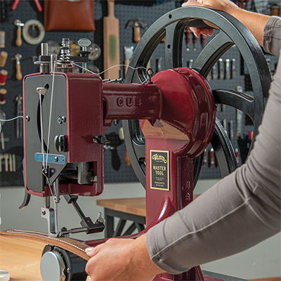 Person operating a Weaver Master Tool sewing machine with leather strap in workshop.