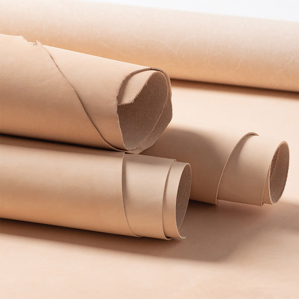Natural veg-tan leather rolls stacked on a flat sheet.